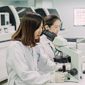 a scientist in lab gear looks down a microscope